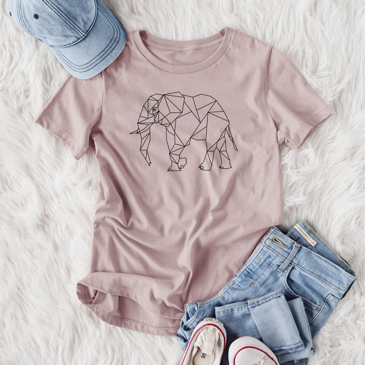 Women's relaxed fit cotton t-shirt printed with a black geometric line art elephant, styled flat on a white faux fur rug with jeans.
