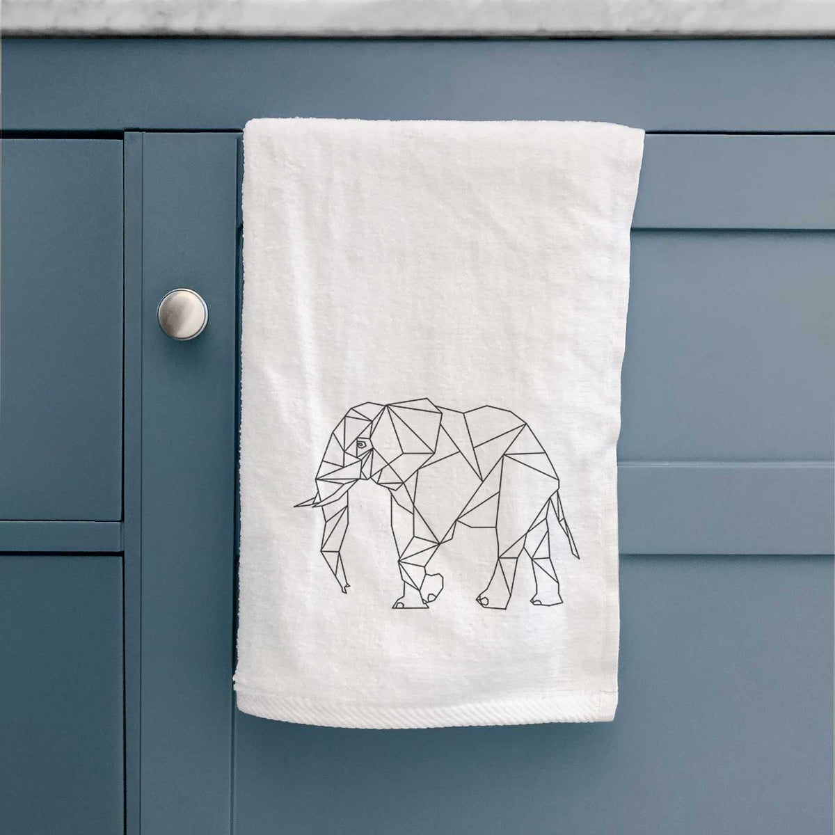 White hand towel printed with a black geometric line art elephant, hanging on a cabinet door.