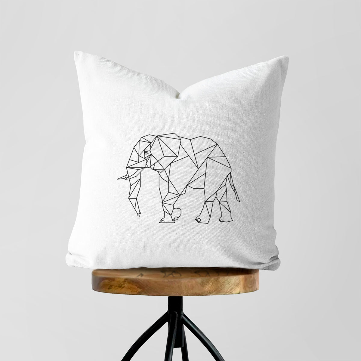 White pillow cover printed with a black geometric line art elephant, on a wooden stool.