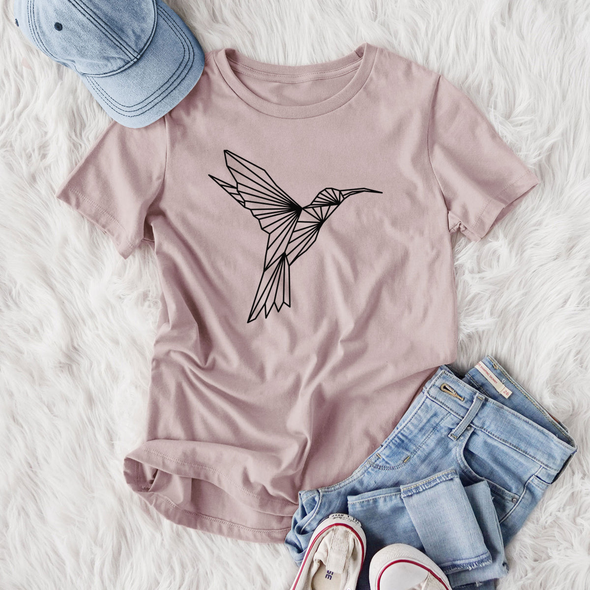Women's relaxed fit cotton t-shirt printed with a black geometric line art hummingbird in flight, styled flat on a white faux fur rug with jeans.