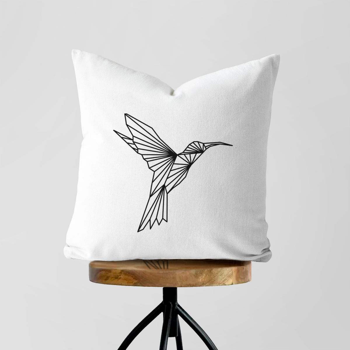 White pillow cover printed with a black geometric line art hummingbird in flight, on a wooden stool.