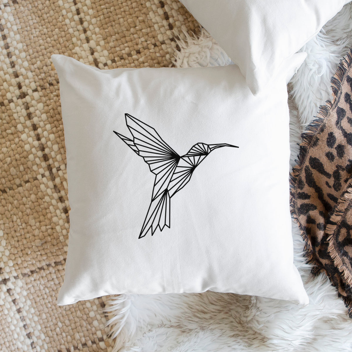 White pillow cover printed with a black geometric line art hummingbird in flight, on a woven chair.