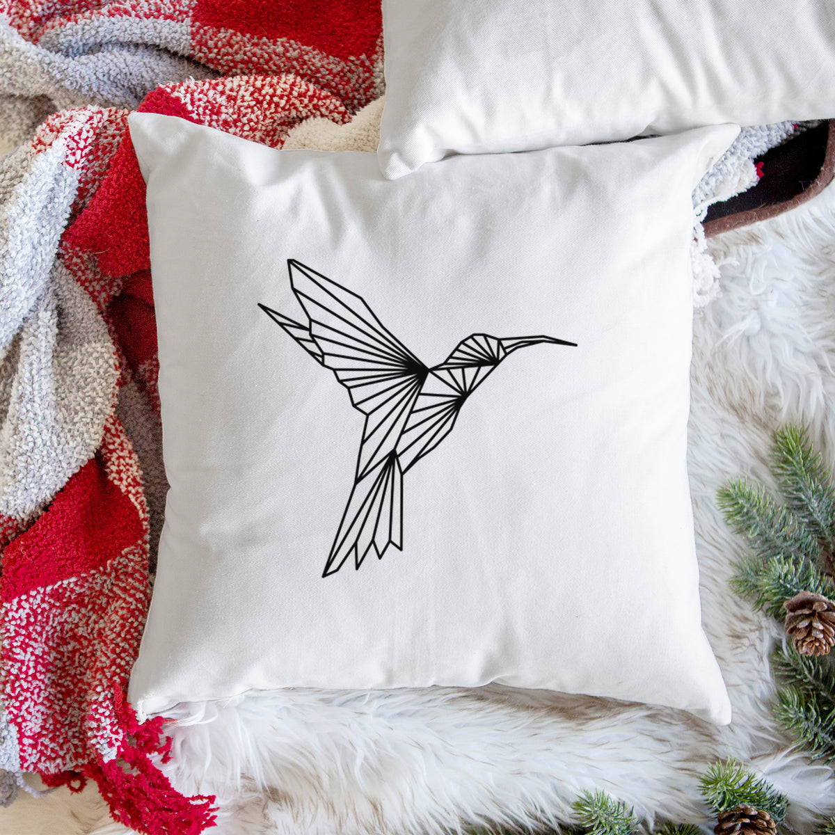 White pillow cover printed with a black geometric line art hummingbird in flight, on a woven chair.
