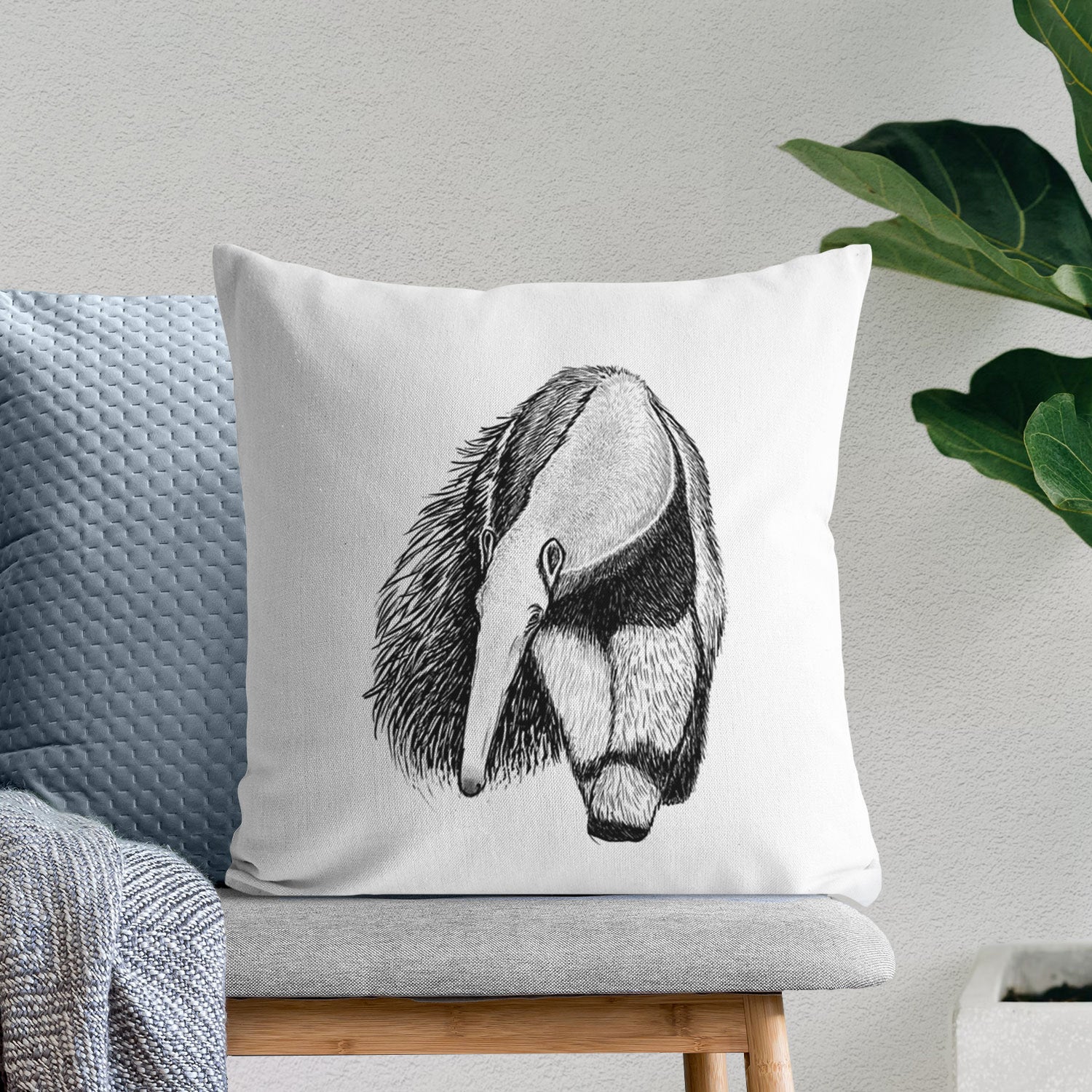 White pillow cover printed with a detailed black ink illustration of a giant anteater with its long snout and bushy tail, on a bench beside plants.