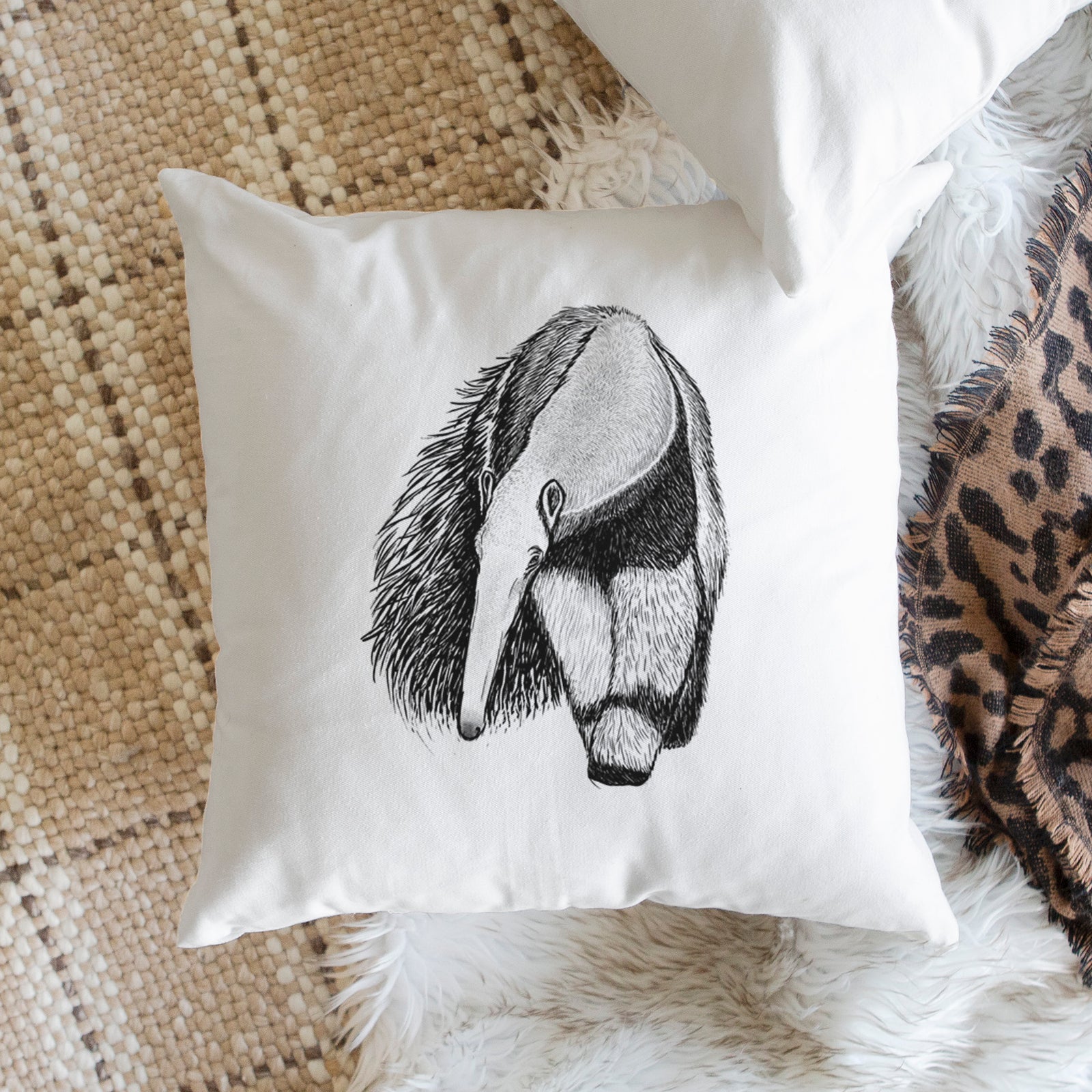 White pillow cover printed with a detailed black ink illustration of a giant anteater with its long snout and bushy tail, on a bench beside plants.