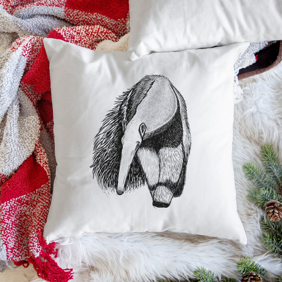 White pillow cover printed with a detailed black ink illustration of a giant anteater with its long snout and bushy tail, on a woven chair.