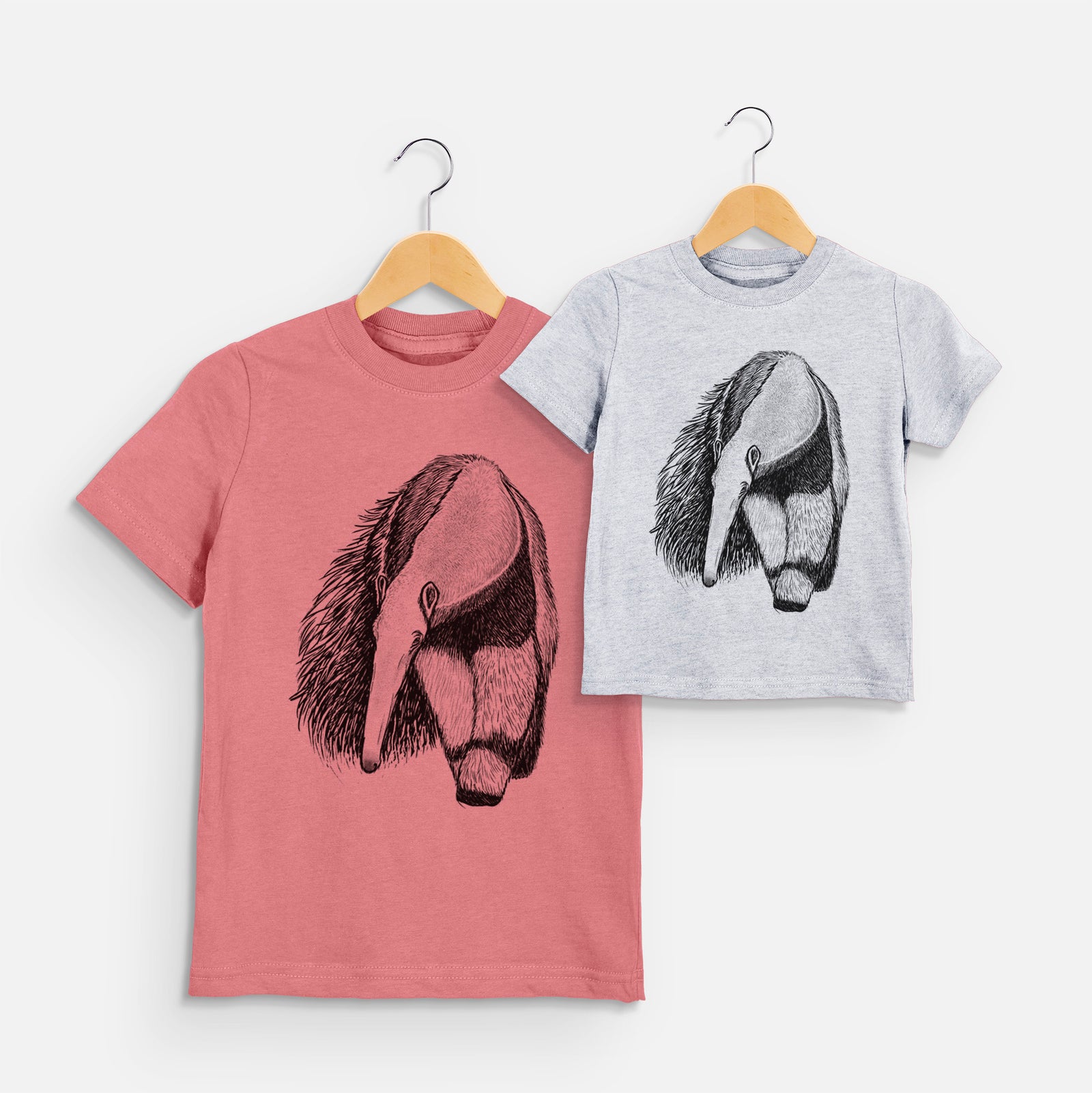 Two youth t-shirts in different colors on hangers, printed with a detailed black ink illustration of a giant anteater with its long snout and bushy tail.