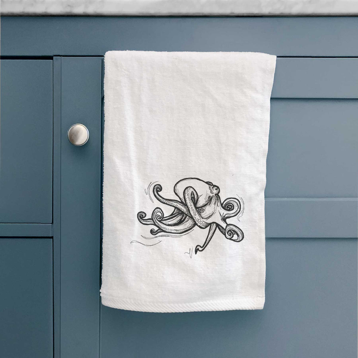 White hand towel printed with a black ink illustration of a giant Pacific octopus with curling tentacles, hanging on a cabinet door.
