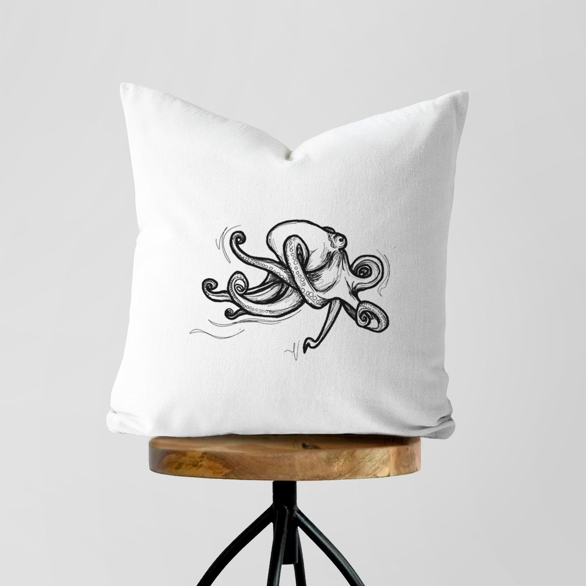 White pillow cover printed with a black ink illustration of a giant Pacific octopus with curling tentacles, on a wooden stool.