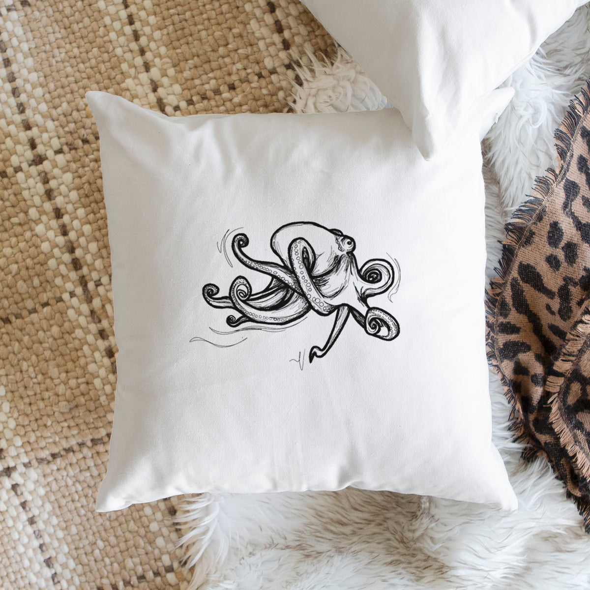 White pillow cover printed with a black ink illustration of a giant Pacific octopus with curling tentacles, on a woven chair.