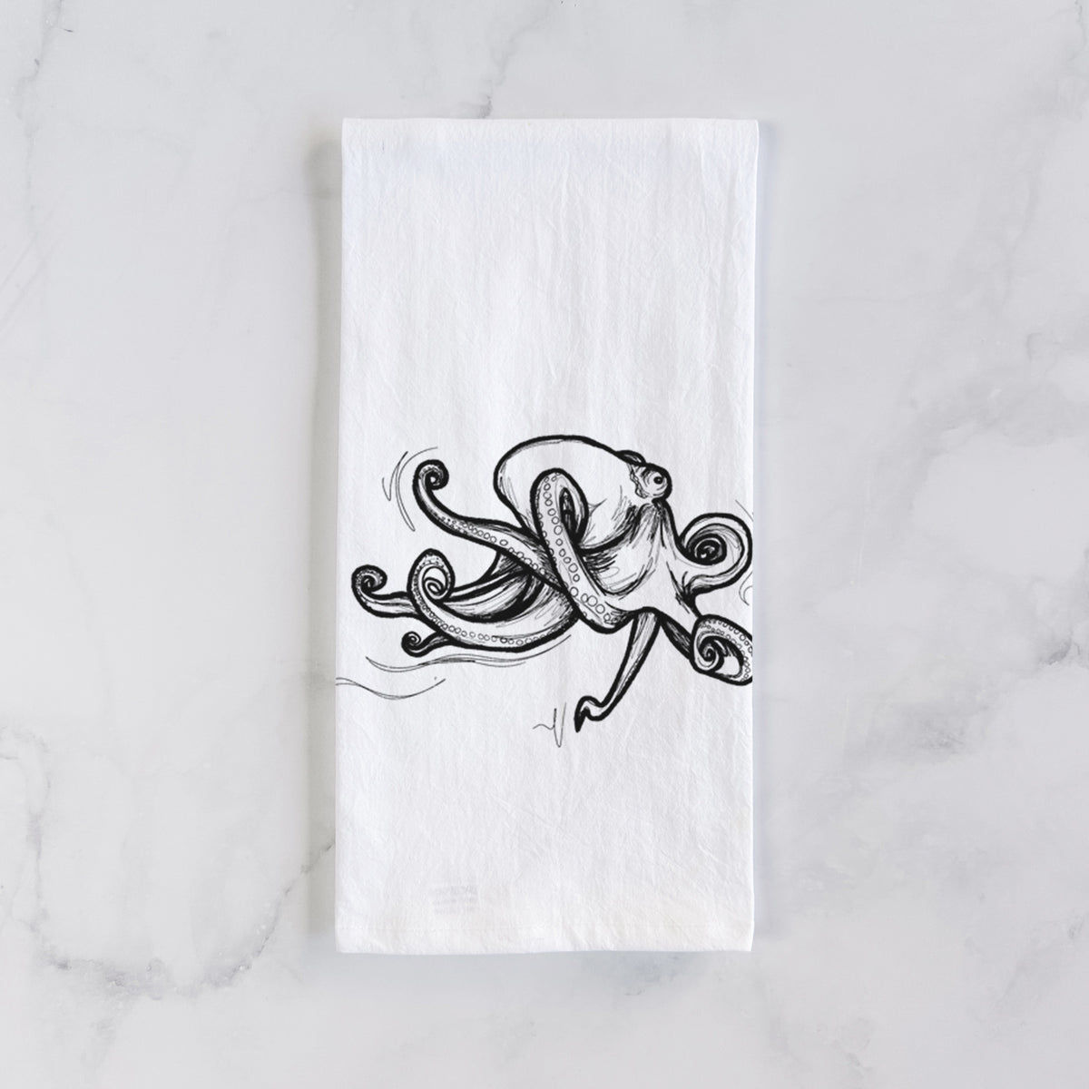 White cotton tea towel laid flat on marble, printed with a black ink illustration of a giant Pacific octopus with curling tentacles.