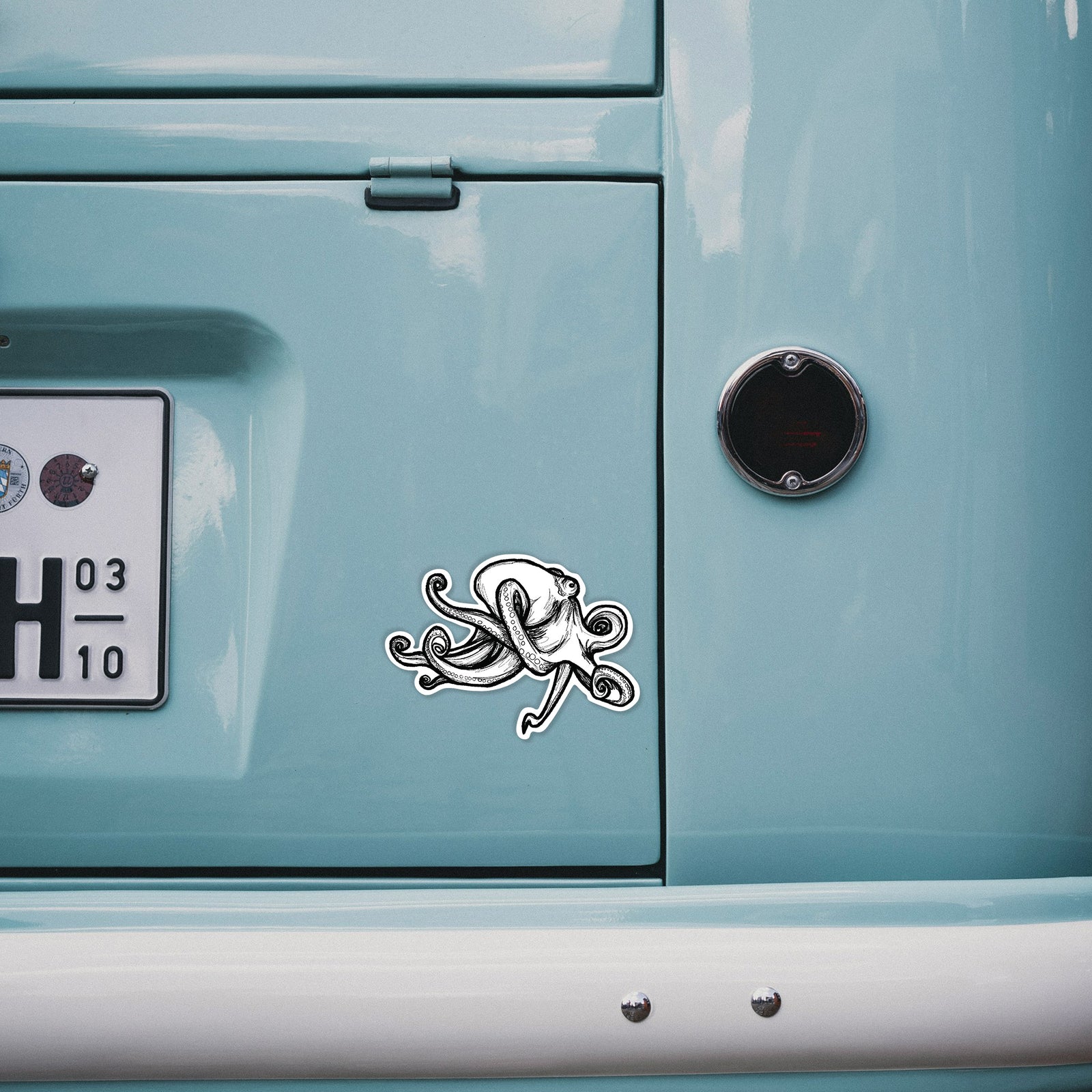 Hand holding a 4 inch vinyl decal of a black ink illustration of a giant Pacific octopus with curling tentacles.