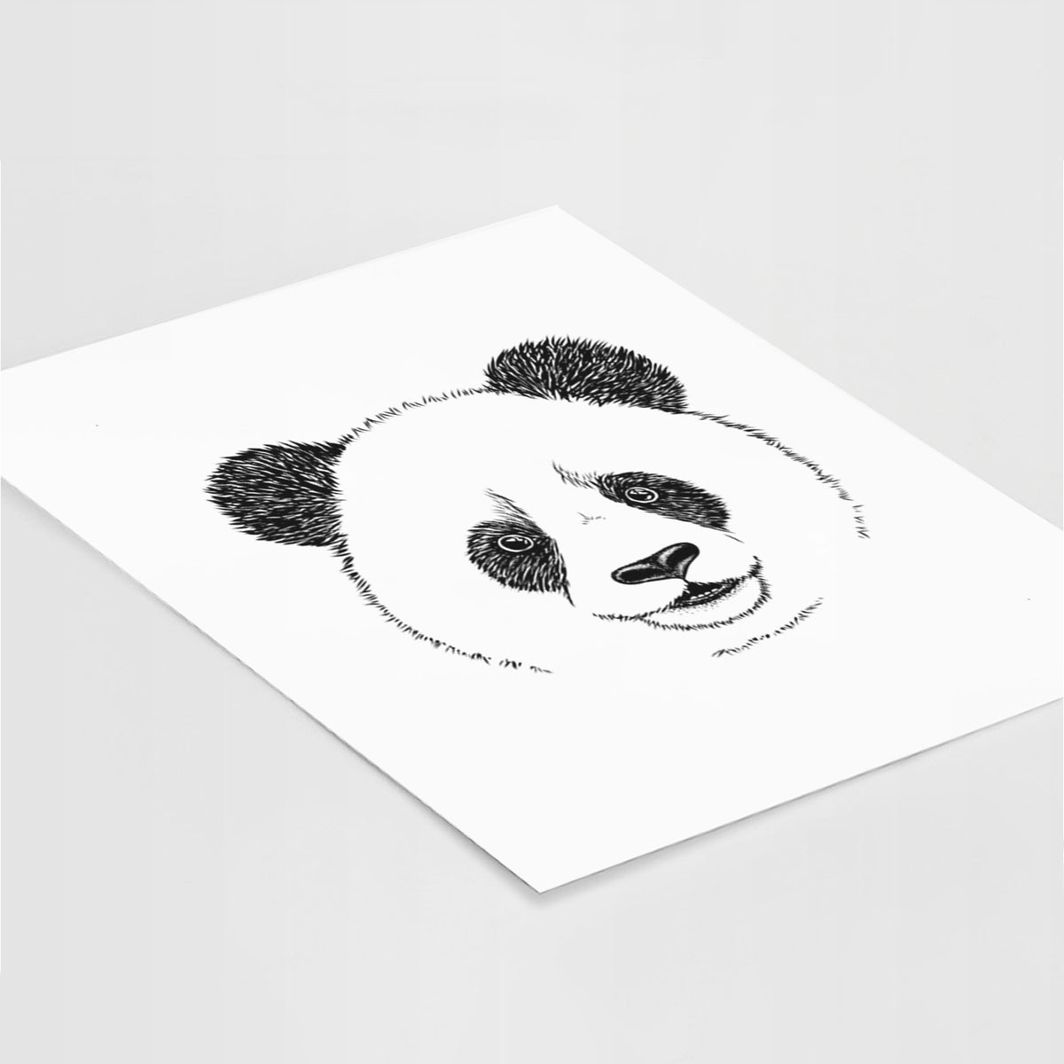 Art print of a black ink portrait of a smiling giant panda's face, lying at an angle on a white surface.