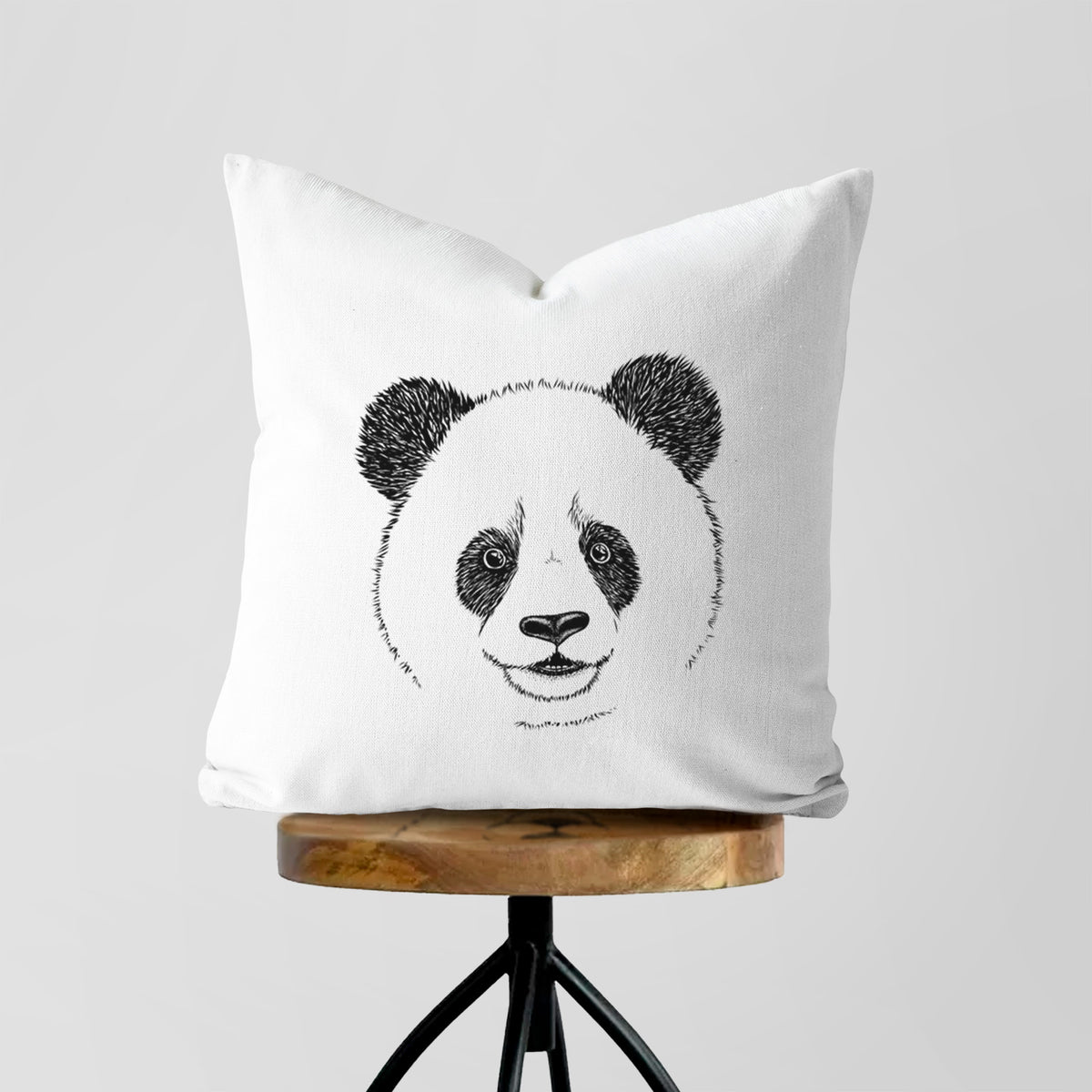 White pillow cover printed with a black ink portrait of a smiling giant panda's face, on a wooden stool.