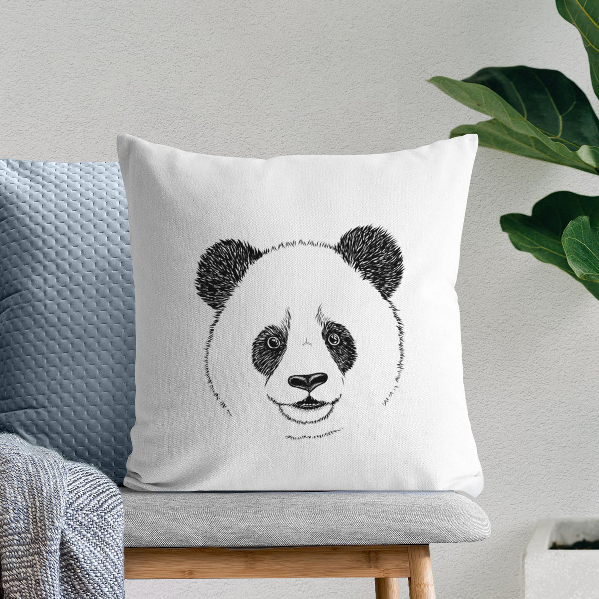 White pillow cover printed with a black ink portrait of a smiling giant panda's face, on a bench beside plants.