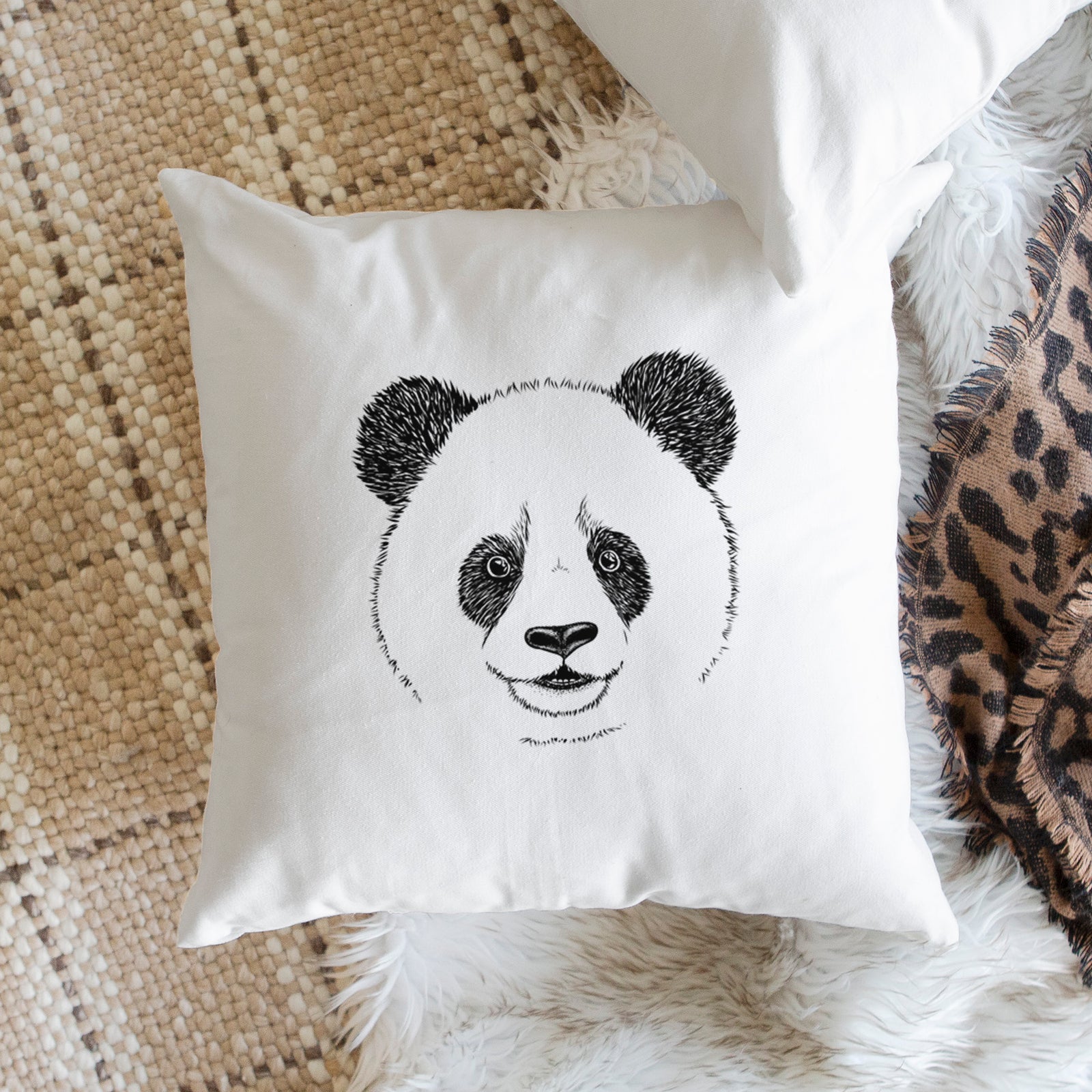 White pillow cover printed with a black ink portrait of a smiling giant panda's face, on a bench beside plants.