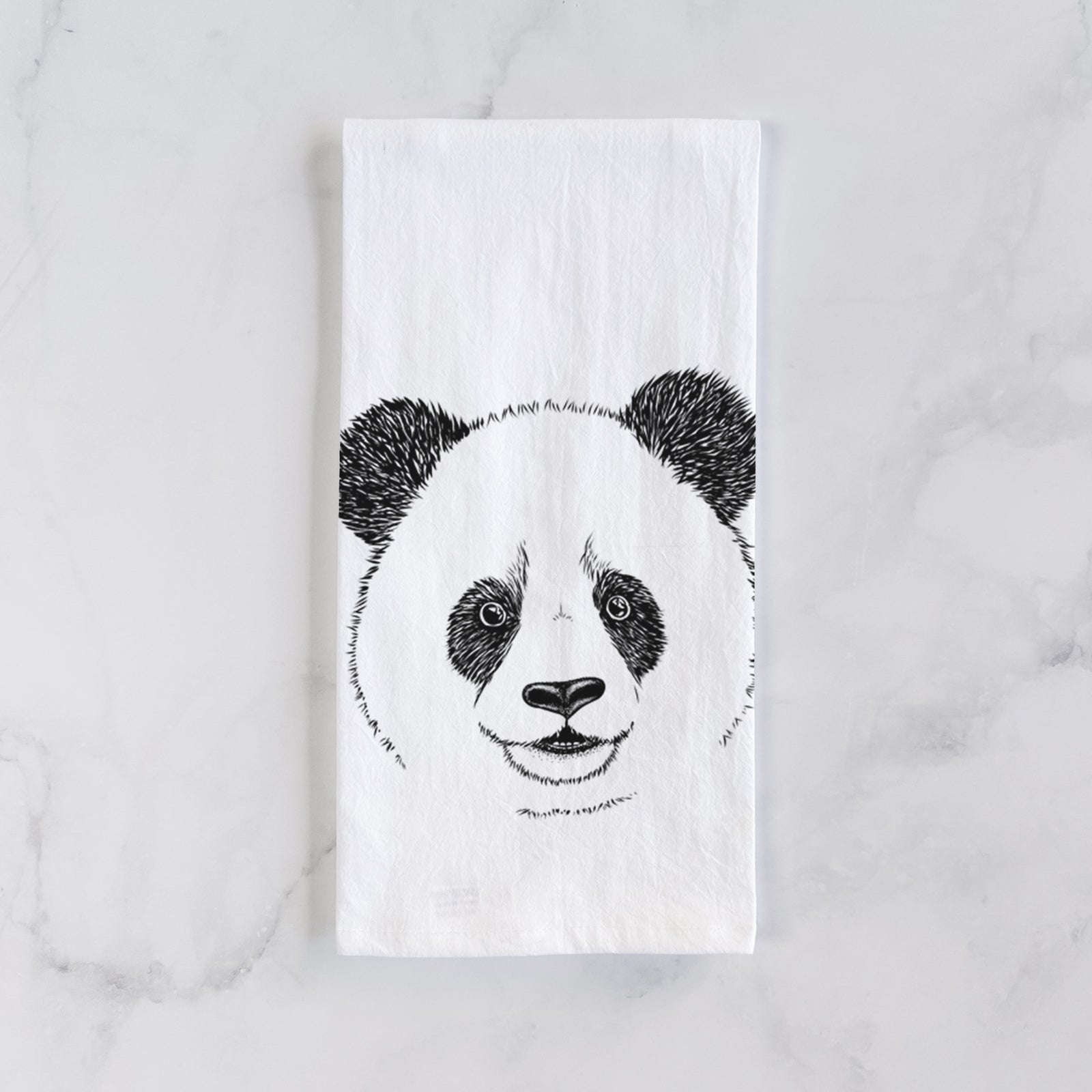 White cotton tea towel printed with a black ink portrait of a smiling giant panda's face, on a marble counter beside a round wooden cutting board and greenery.