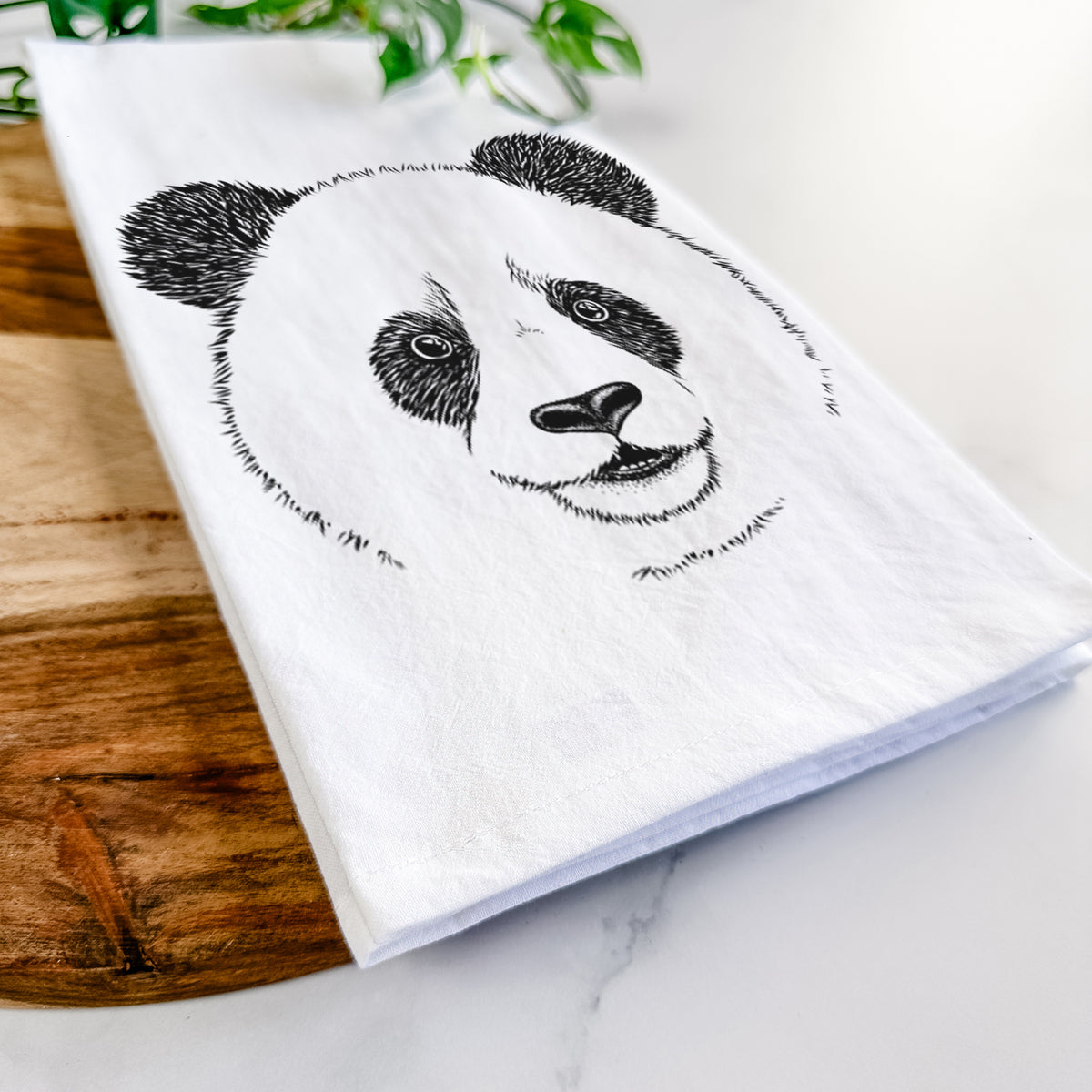 Close-up of a folded white tea towel on a wooden board, showing a black ink portrait of a smiling giant panda's face.