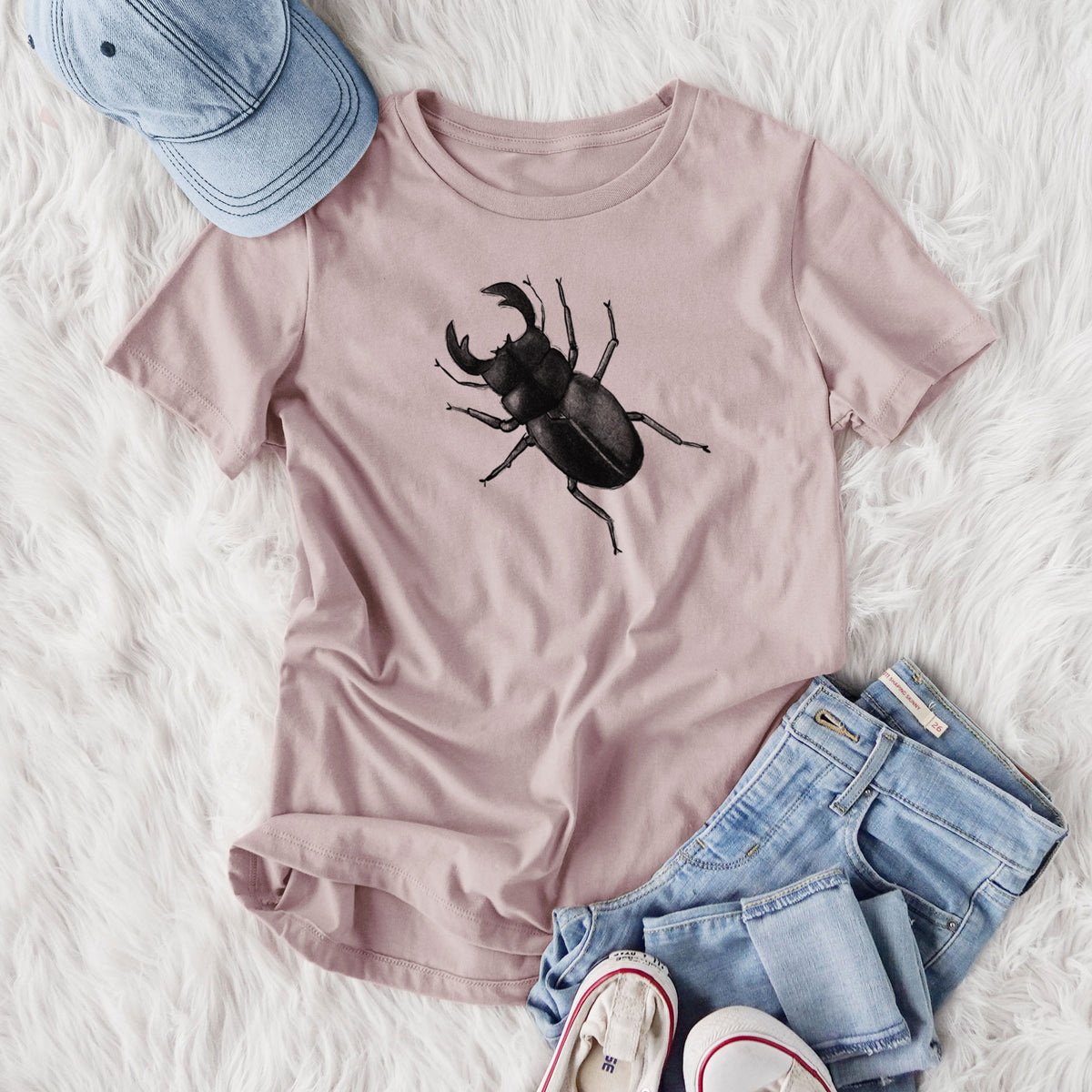 Women's relaxed fit cotton t-shirt printed with a detailed black ink illustration of a giant stag beetle with large jaws, seen from above, styled flat on a white faux fur rug with jeans.