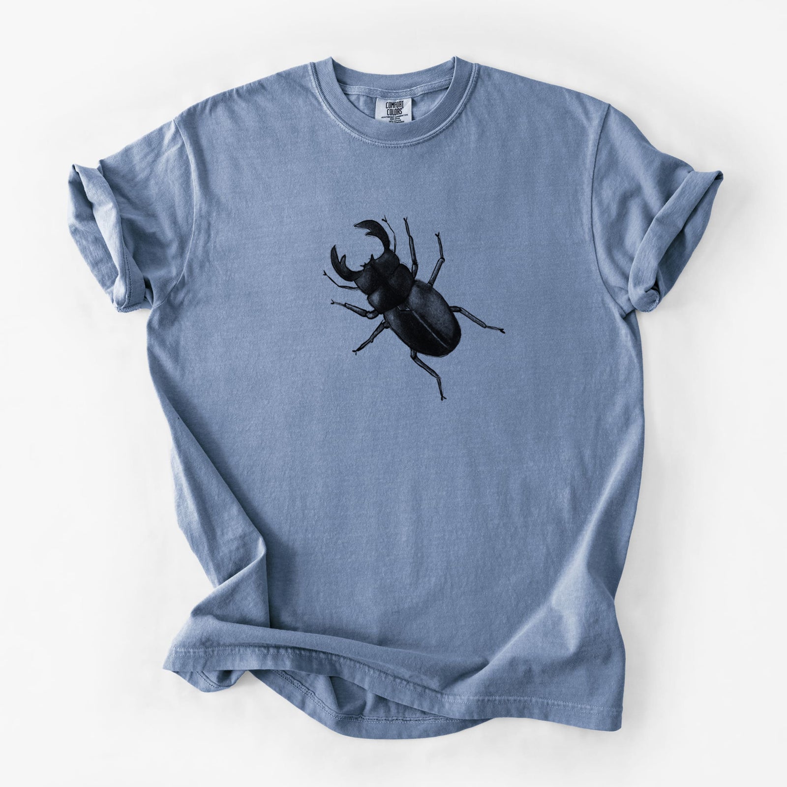 Blue jean Comfort Colors t-shirt laid flat, printed with a detailed black ink illustration of a giant stag beetle with large jaws, seen from above.