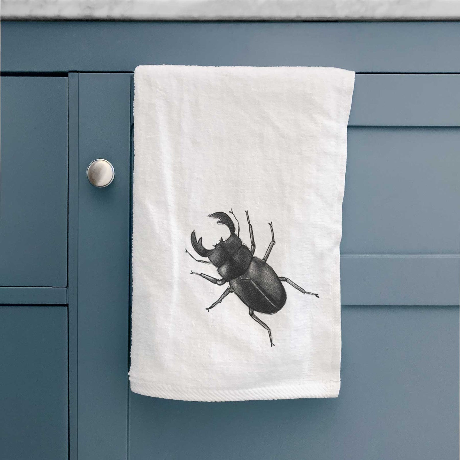 White hand towel printed with a detailed black ink illustration of a giant stag beetle with large jaws, seen from above.