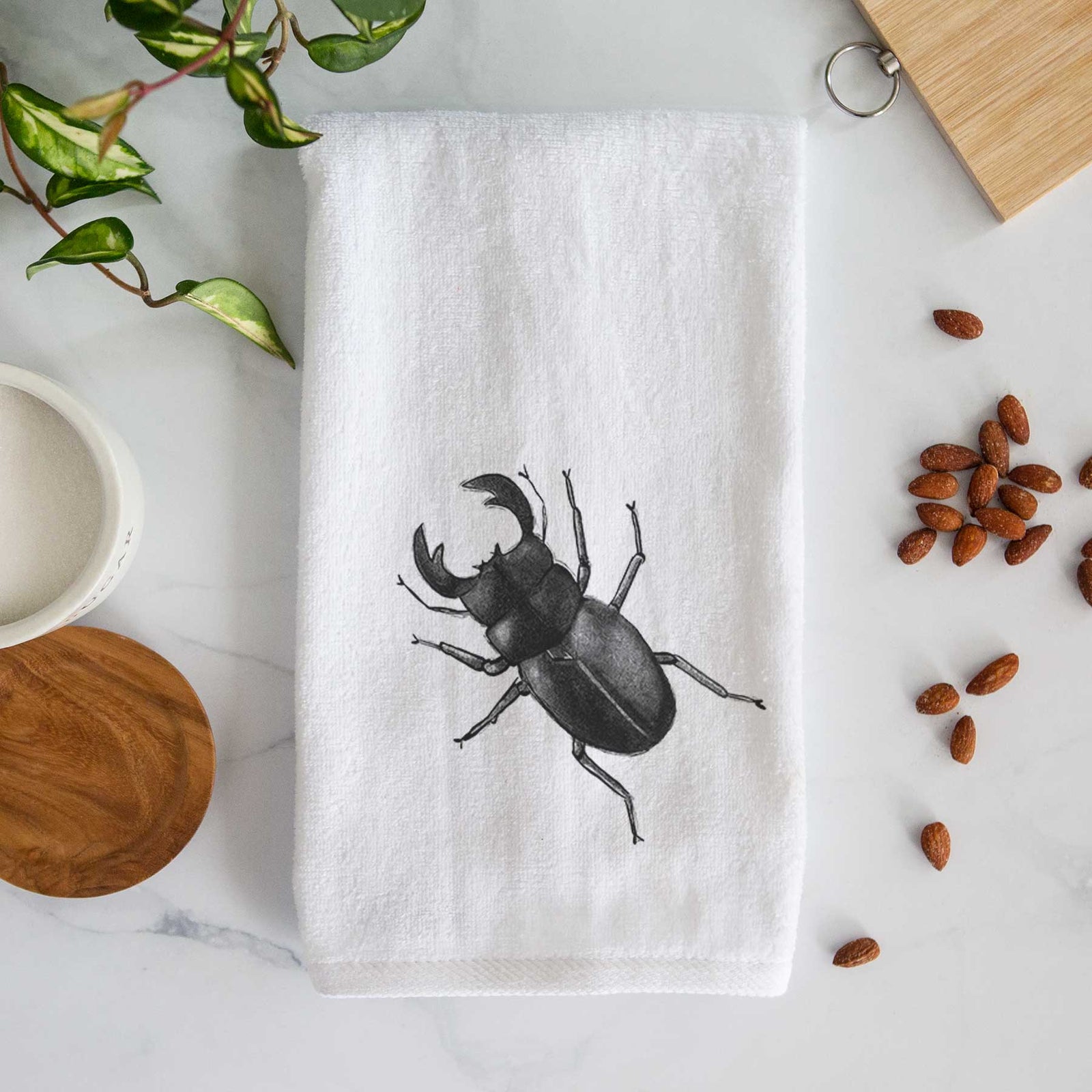 White hand towel printed with a detailed black ink illustration of a giant stag beetle with large jaws, seen from above.