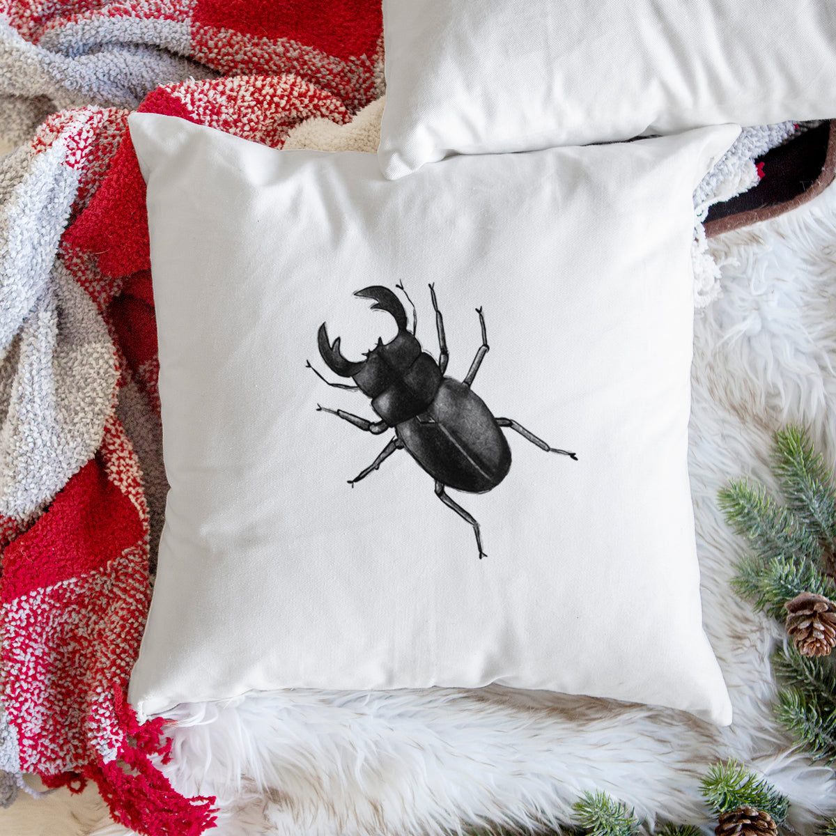 White pillow cover printed with a detailed black ink illustration of a giant stag beetle with large jaws, seen from above, on a woven chair.