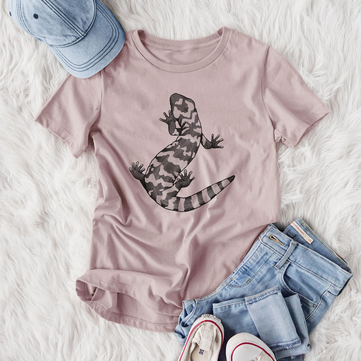 Women's relaxed fit cotton t-shirt printed with a black ink illustration of a Gila monster with bold patterned skin, styled flat on a white faux fur rug with jeans.