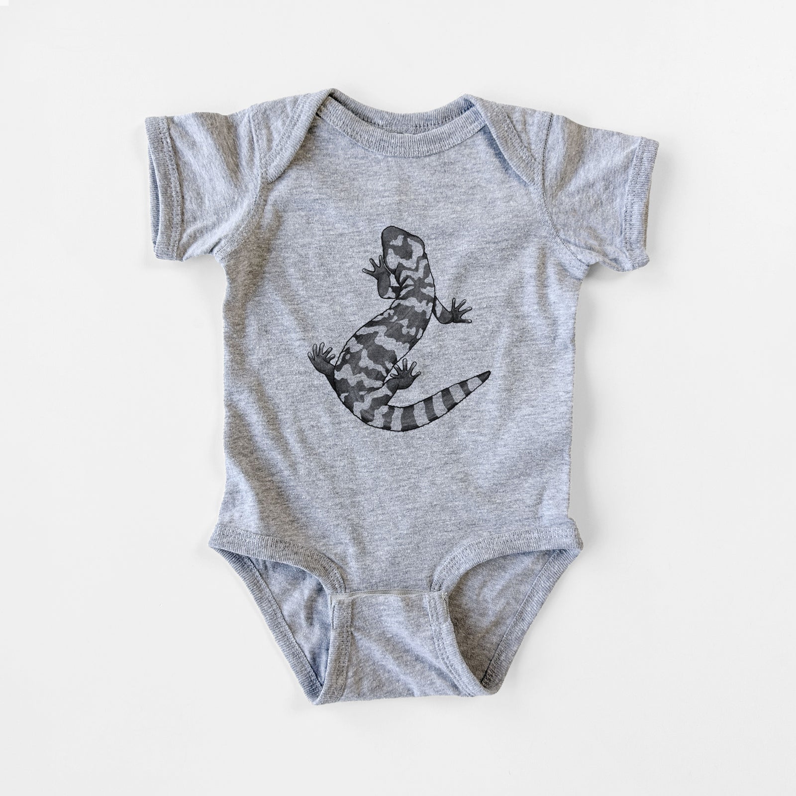 Grey baby bodysuit laid flat, printed with a black ink illustration of a Gila monster with bold patterned skin.