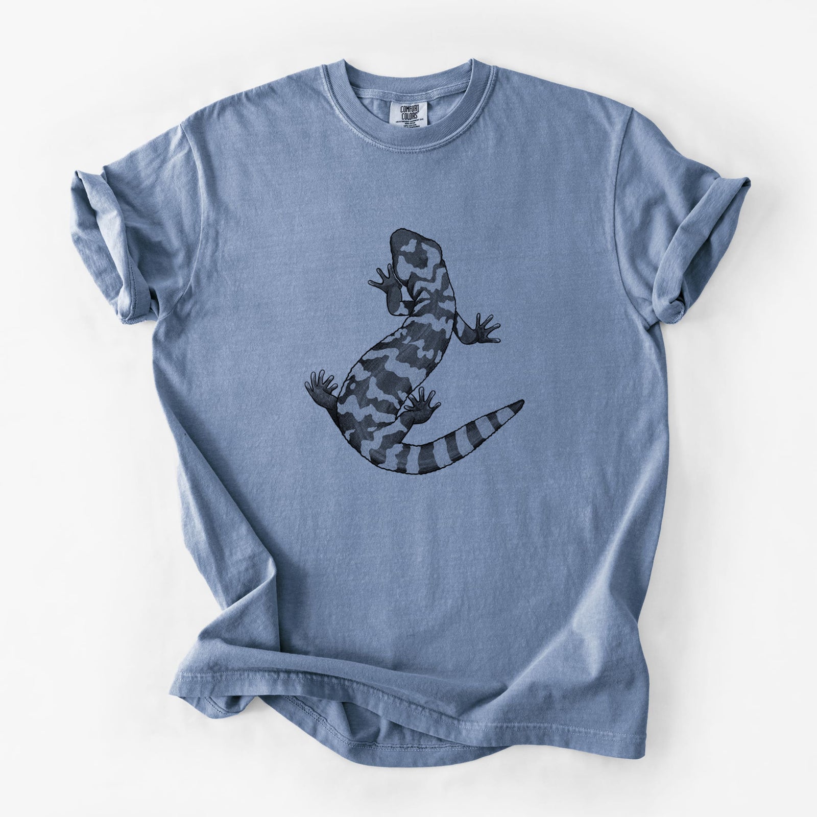 Blue jean Comfort Colors t-shirt laid flat, printed with a black ink illustration of a Gila monster with bold patterned skin.