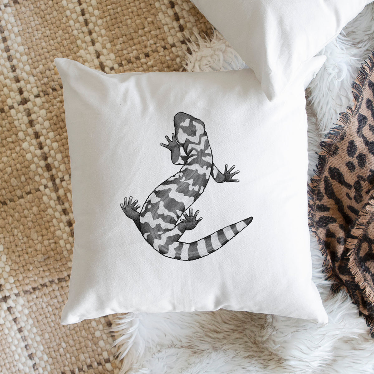 White pillow cover printed with a black ink illustration of a Gila monster with bold patterned skin, on a woven chair.