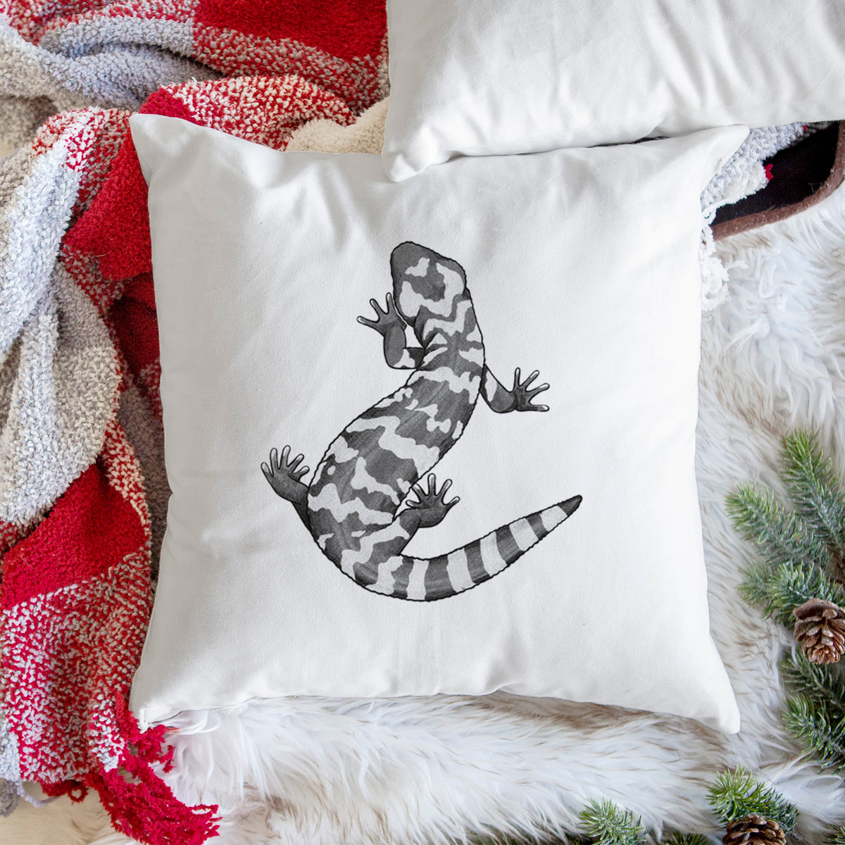 White pillow cover printed with a black ink illustration of a Gila monster with bold patterned skin, on a woven chair.