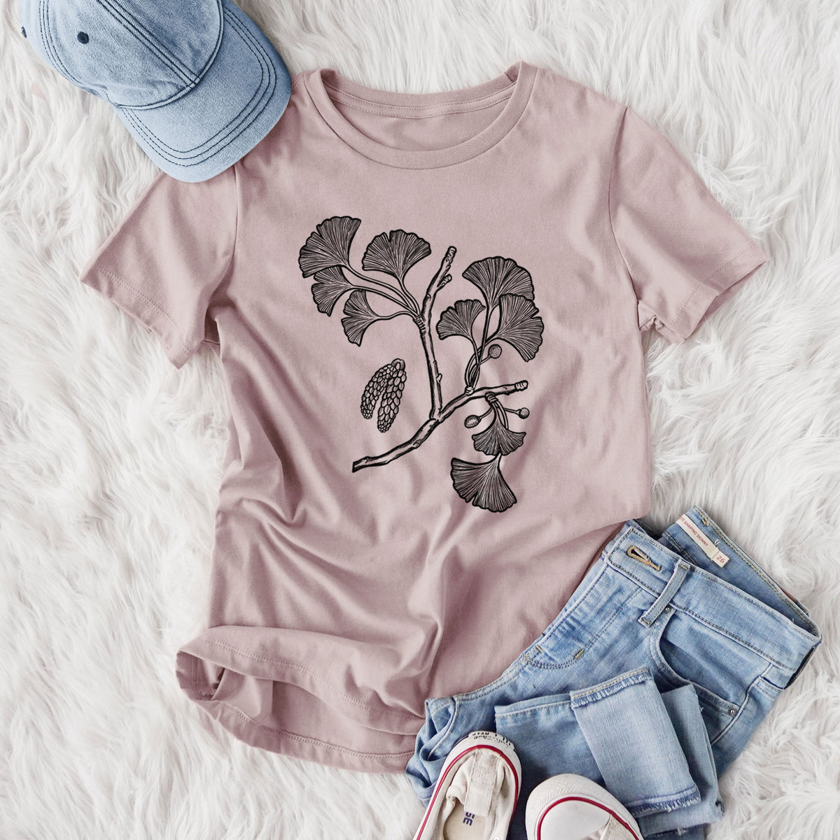Women's relaxed fit cotton t-shirt printed with a black ink illustration of a ginkgo branch with fan-shaped leaves, styled flat on a white faux fur rug with jeans.