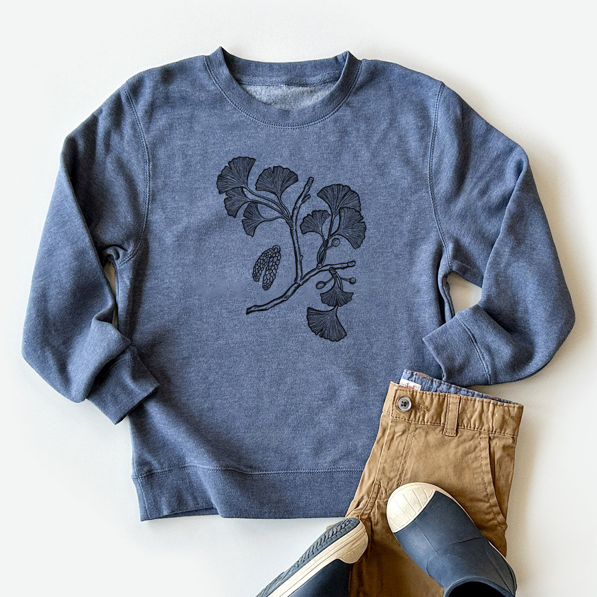 Youth crewneck sweatshirt printed with a black ink illustration of a ginkgo branch with fan-shaped leaves, styled flat with khaki pants and shoes.