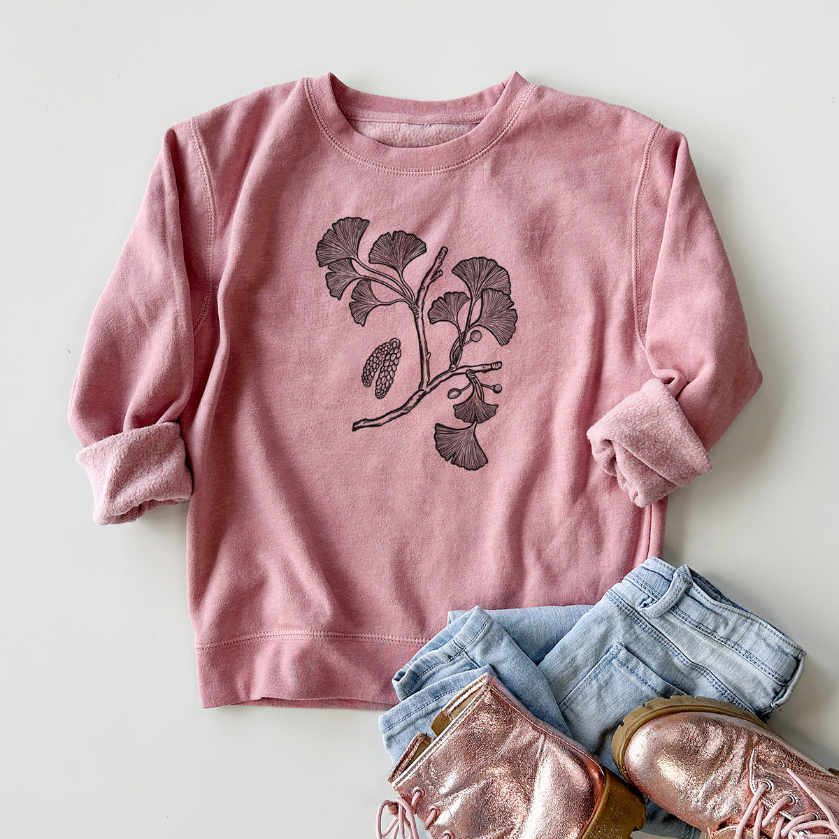 Youth crewneck sweatshirt printed with a black ink illustration of a ginkgo branch with fan-shaped leaves, styled flat with jeans and boots.