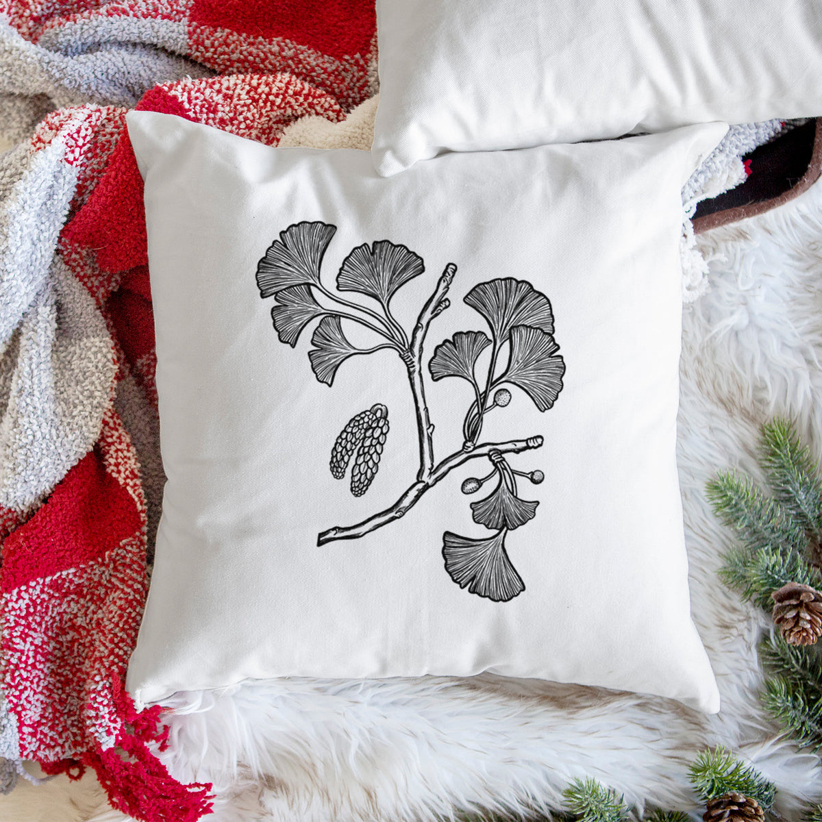 White pillow cover printed with a black ink illustration of a ginkgo branch with fan-shaped leaves, on a woven chair.