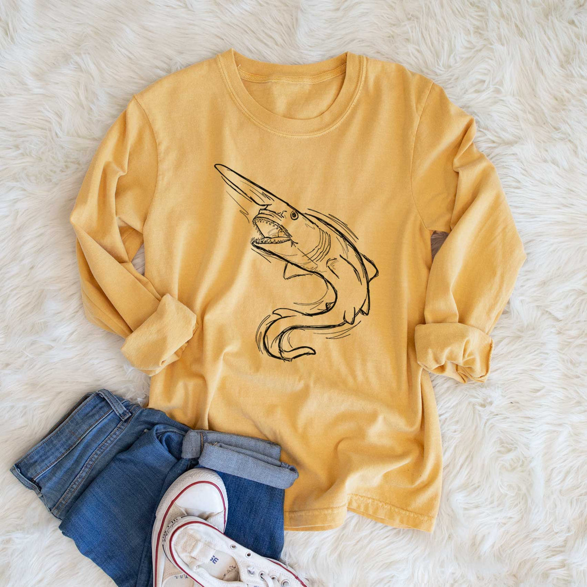 Golden wheat yellow Comfort Colors long sleeve shirt printed with a black ink illustration of a goblin shark with its long snout, swimming in a curve, shown in a lifestyle photo.