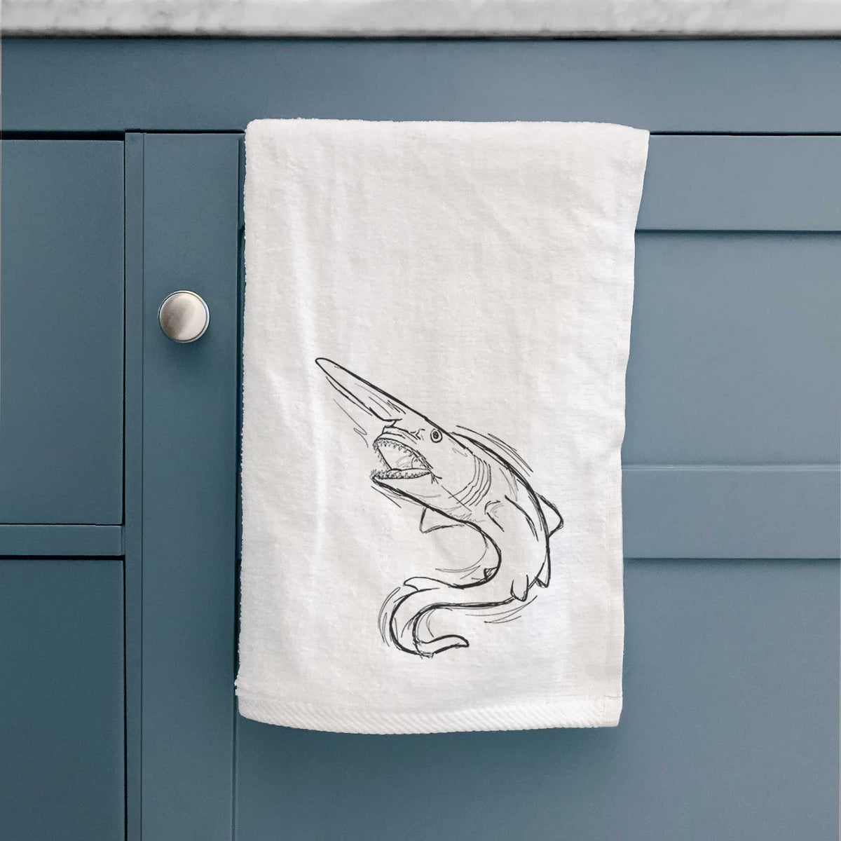 White hand towel printed with a black ink illustration of a goblin shark with its long snout, swimming in a curve, hanging on a cabinet door.