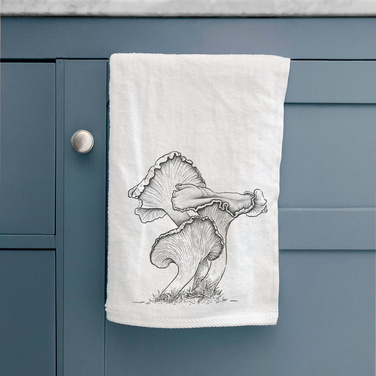 White hand towel printed with a detailed black ink illustration of golden chanterelle mushrooms, hanging on a cabinet door.
