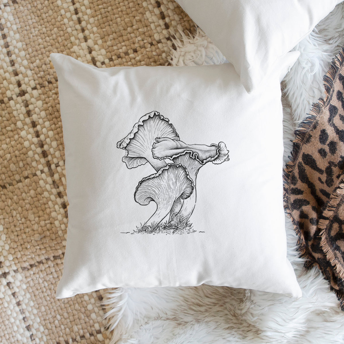 White pillow cover printed with a detailed black ink illustration of golden chanterelle mushrooms, on a woven chair.