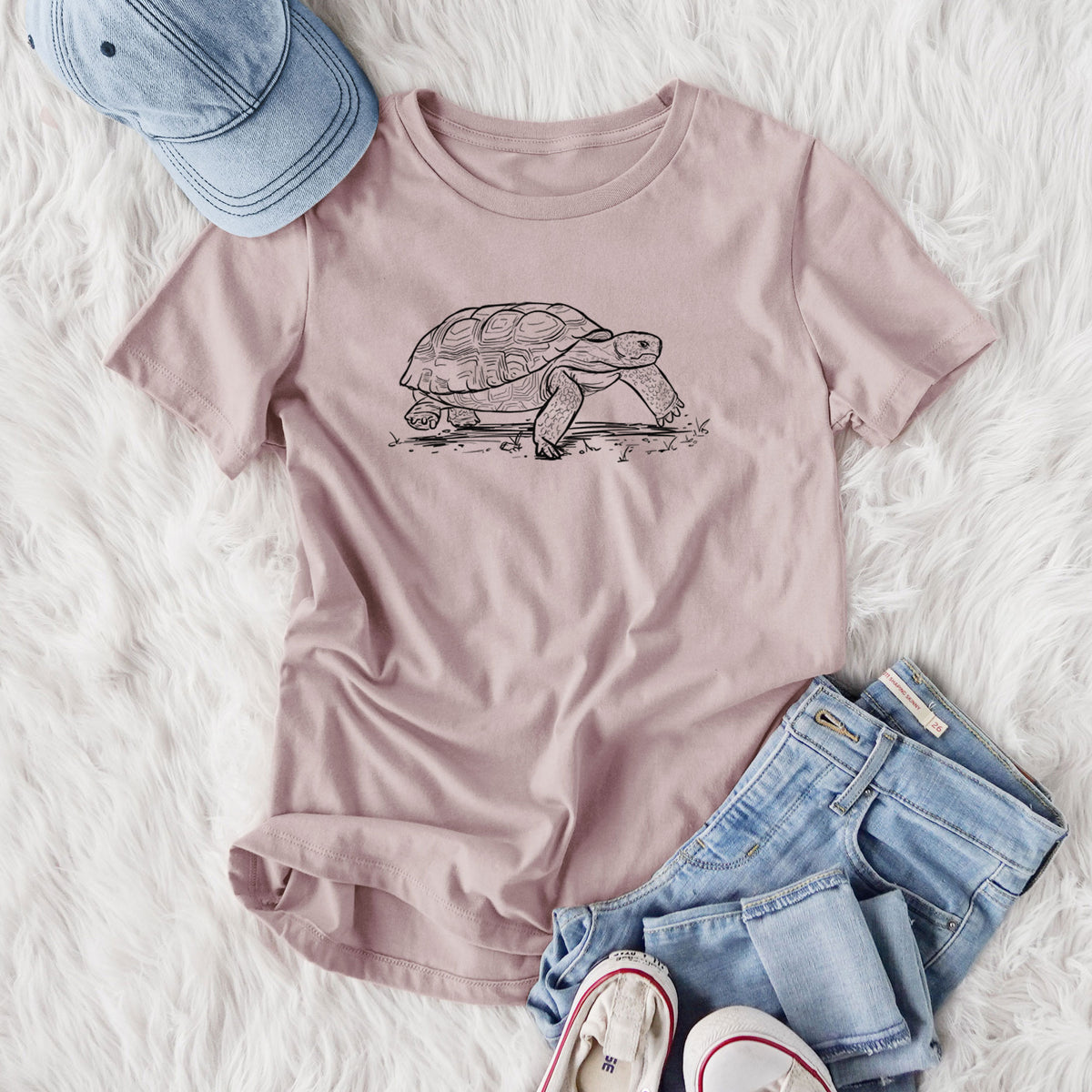 Women's relaxed fit cotton t-shirt printed with a detailed black ink illustration of a gopher tortoise walking, styled flat on a white faux fur rug with jeans.