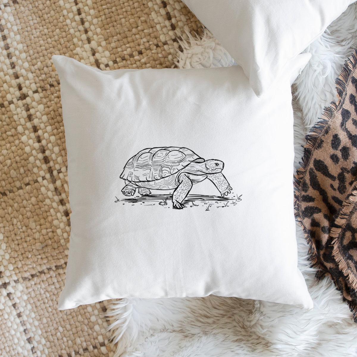 White pillow cover printed with a detailed black ink illustration of a gopher tortoise walking, on a woven chair.