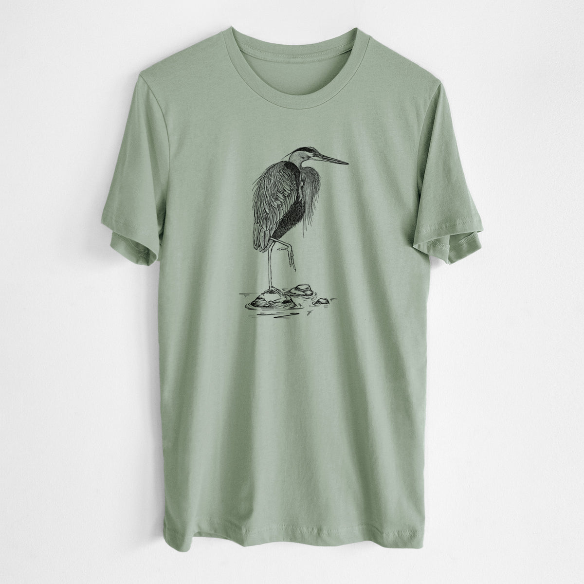 Sage green lightweight cotton t-shirt laid flat, printed with a detailed black ink illustration of a great blue heron standing on rocks.