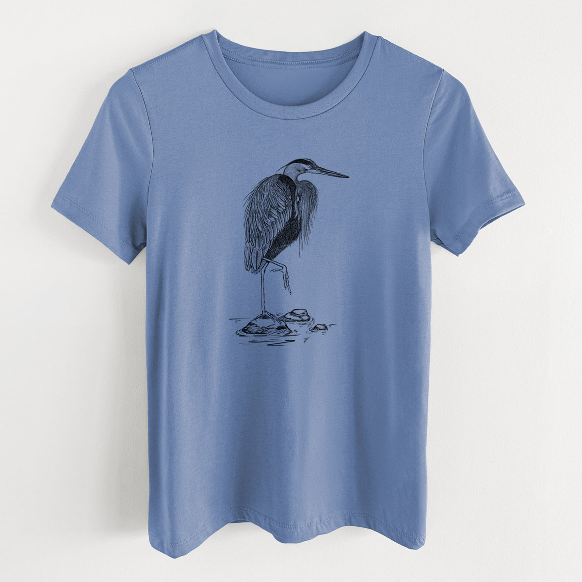 Blue bell women's relaxed fit cotton t-shirt laid flat, printed with a detailed black ink illustration of a great blue heron standing on rocks.