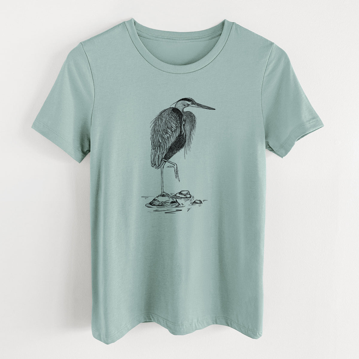 Dusty blue women's relaxed fit cotton t-shirt laid flat, printed with a detailed black ink illustration of a great blue heron standing on rocks.