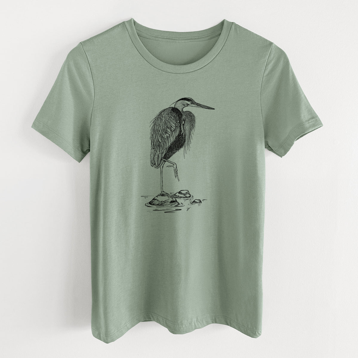 Sage green women's relaxed fit cotton t-shirt laid flat, printed with a detailed black ink illustration of a great blue heron standing on rocks.