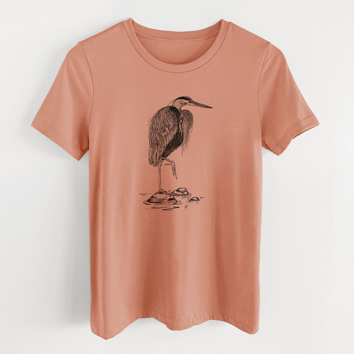 Terracotta orange women's relaxed fit cotton t-shirt laid flat, printed with a detailed black ink illustration of a great blue heron standing on rocks.
