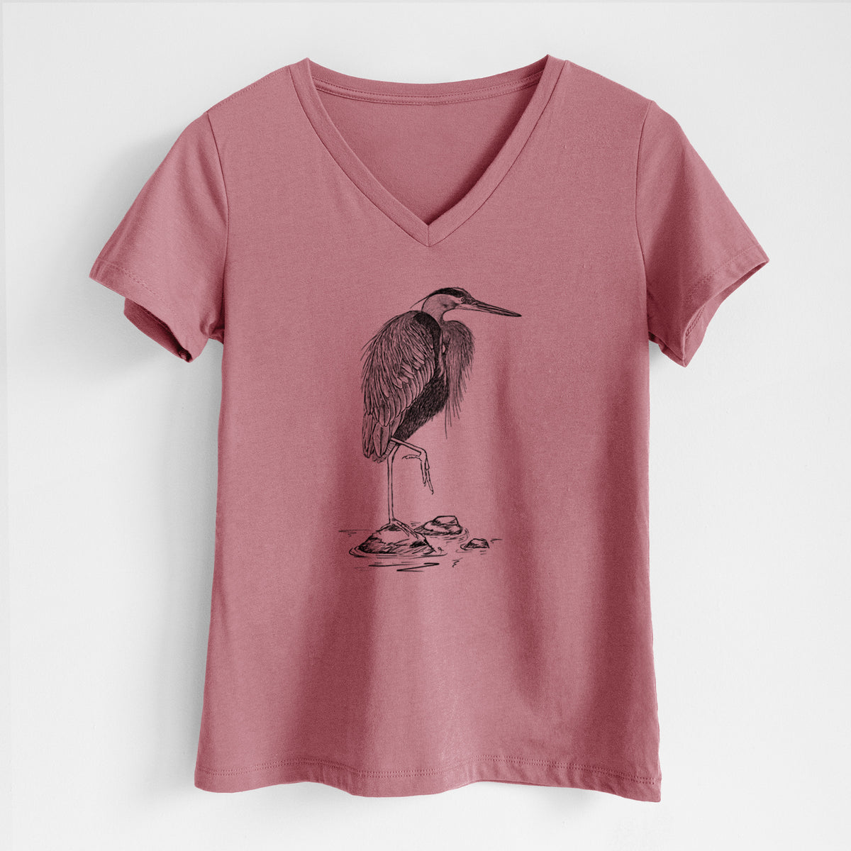 Mauve pink women's relaxed fit cotton V-neck t-shirt laid flat, printed with a detailed black ink illustration of a great blue heron standing on rocks.