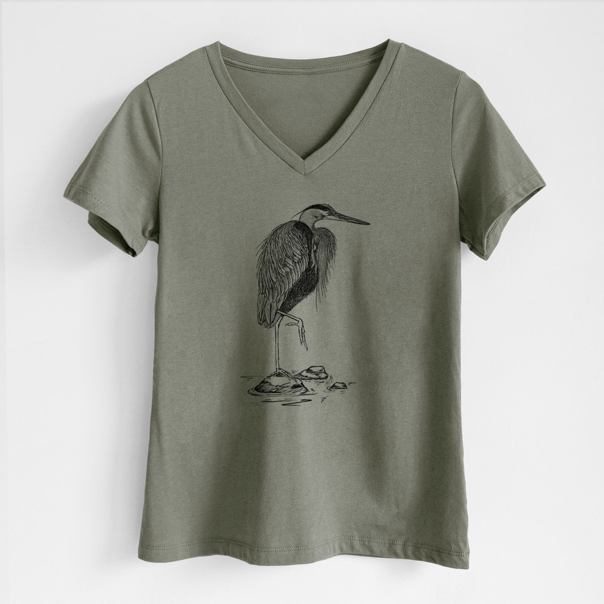 Military green women's relaxed fit cotton V-neck t-shirt laid flat, printed with a detailed black ink illustration of a great blue heron standing on rocks.