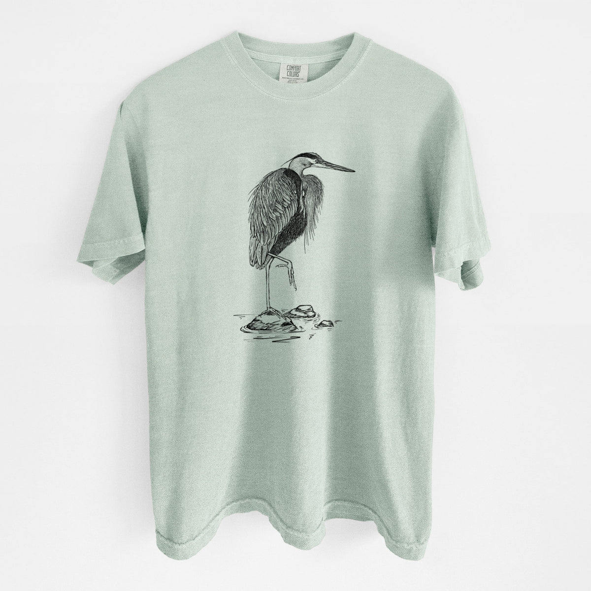Bay green Comfort Colors t-shirt laid flat, printed with a detailed black ink illustration of a great blue heron standing on rocks.